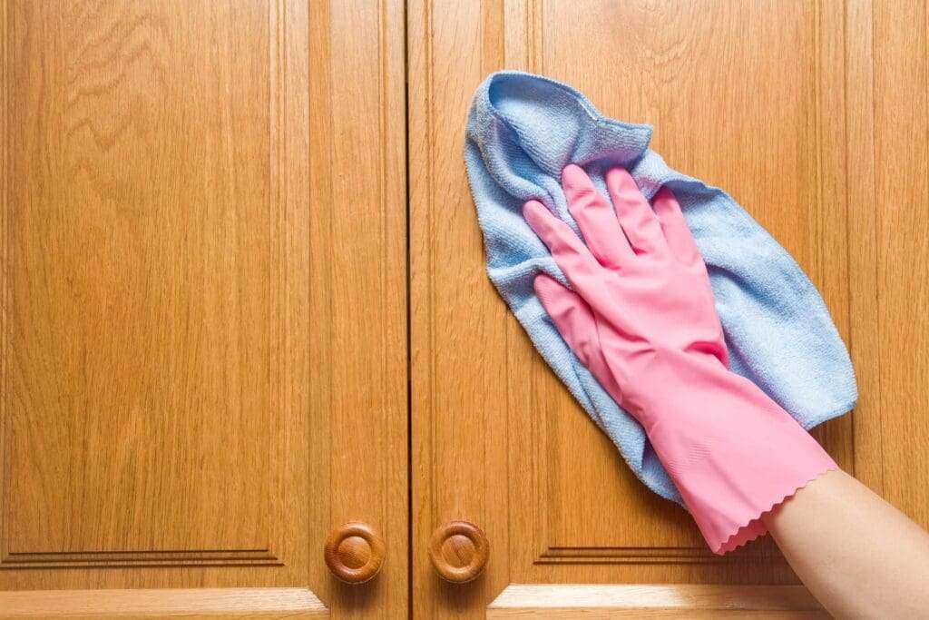 close shot of a hand wearing pink gloves and cleaning wardrobe with cloth.