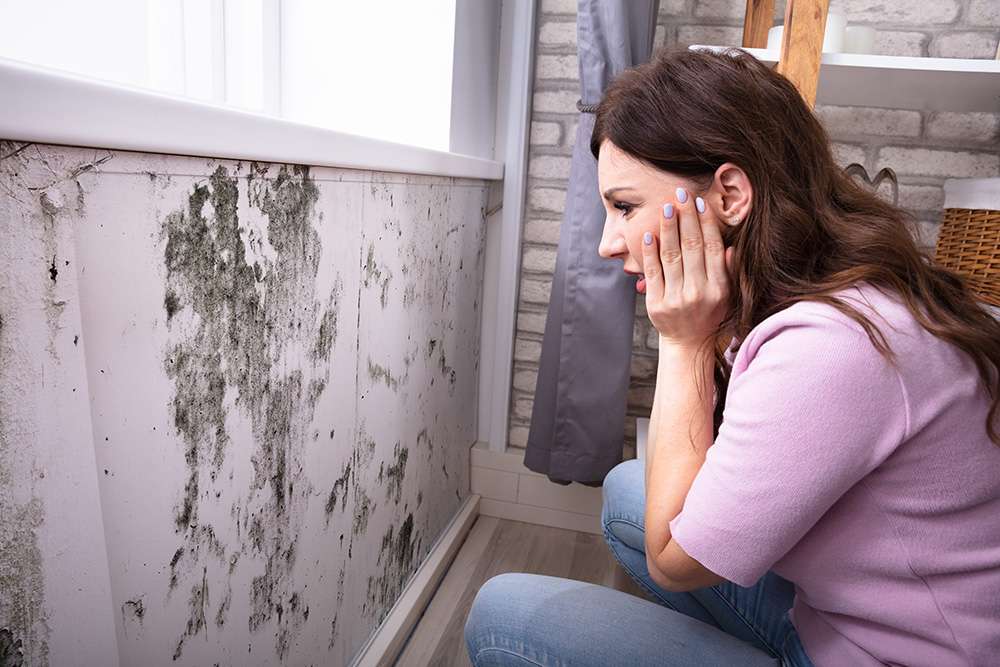 woman looking worried after seeing mold on wall.