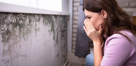 a woman is looking worried after seeing mold on wall.